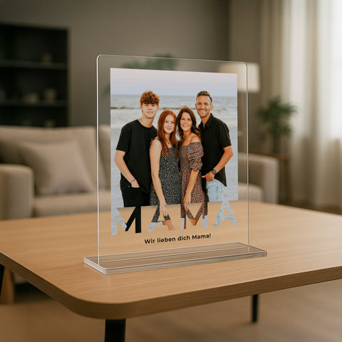 mumaboard MAMA Acrylglas Fotogeschenk mit Familienfoto am Strand und personalisiertem Spruch „Wir lieben dich Mama" auf einem Tisch im Wohnzimmer