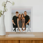 mumaboard MAMA Acrylglas Fotogeschenk mit Familienfoto am Strand und personalisiertem Spruch „Wir lieben dich Mama" neben einer Vase mit Kirschblütenzweig